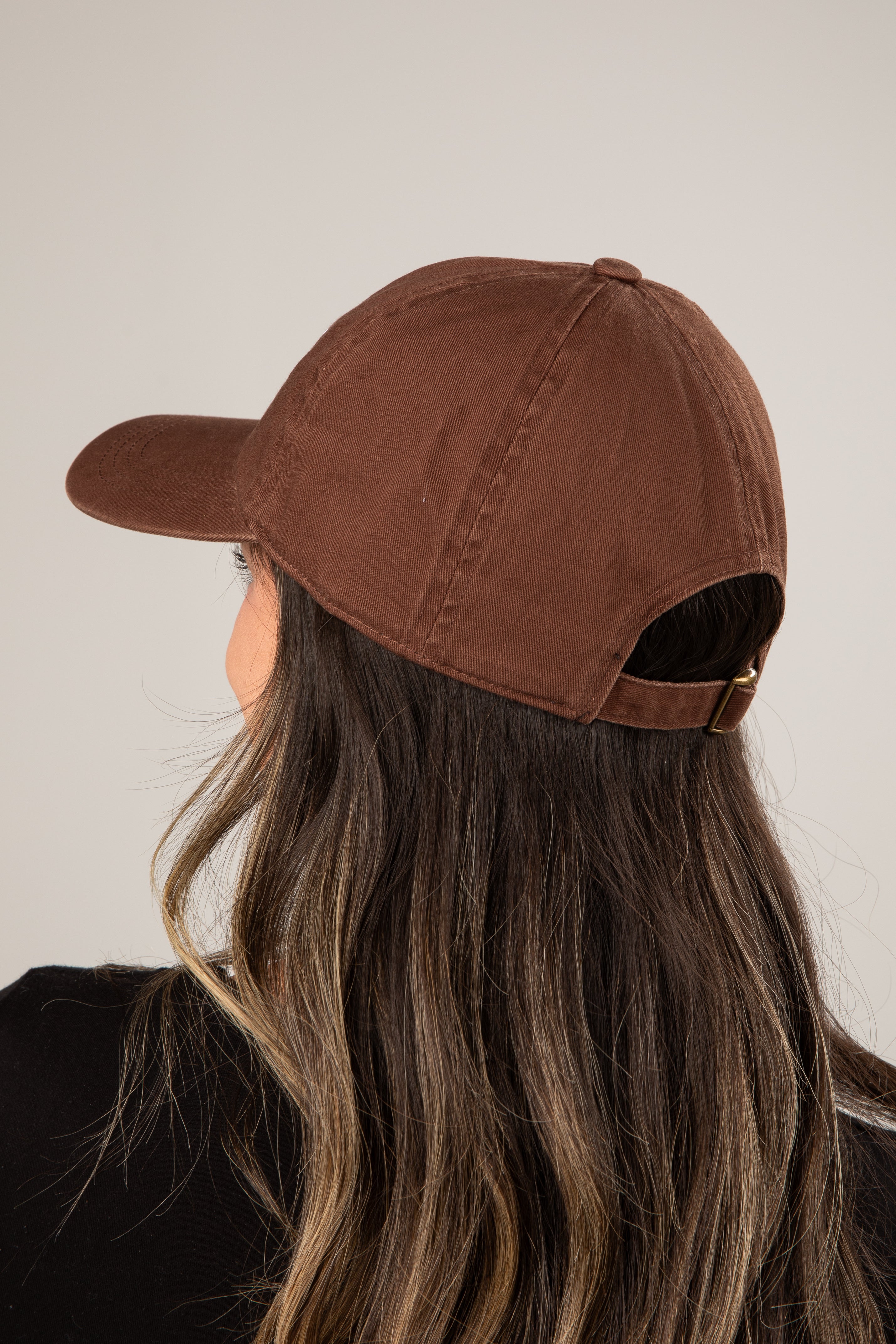 Brown cap worn by a person with long hair against a neutral background