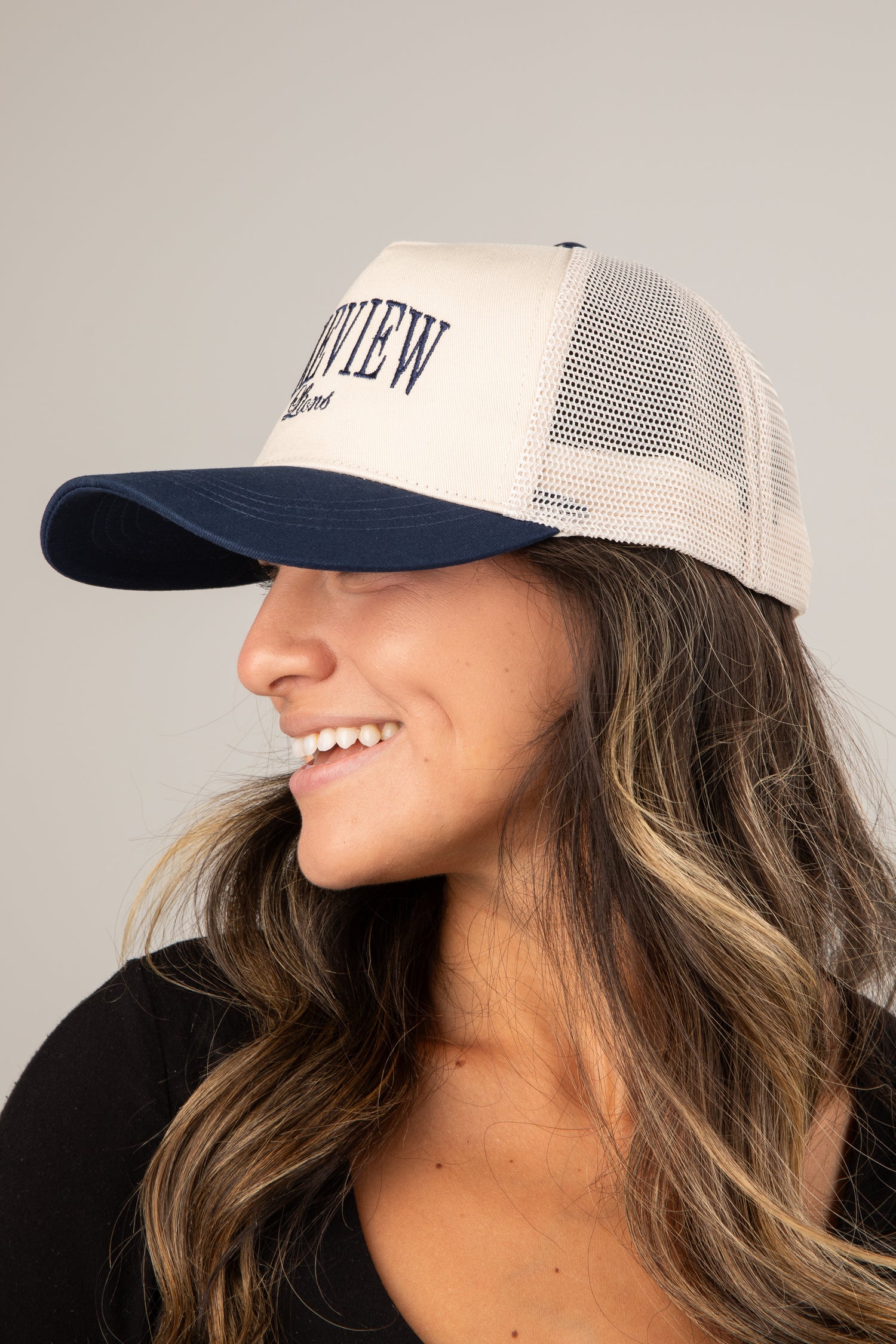 Woman wearing a beige and navy trucker cap with &