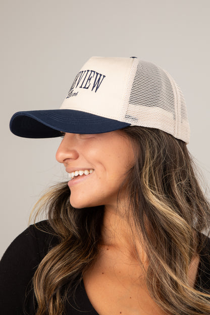 Woman wearing a beige and navy trucker cap with &