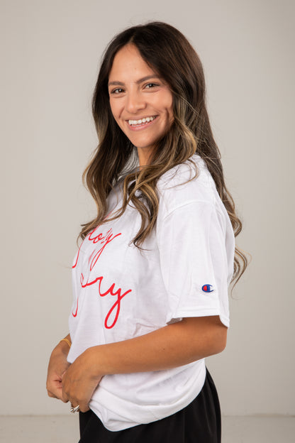 Woman wearing a white t-shirt with red text and a logo, standing against a plain background