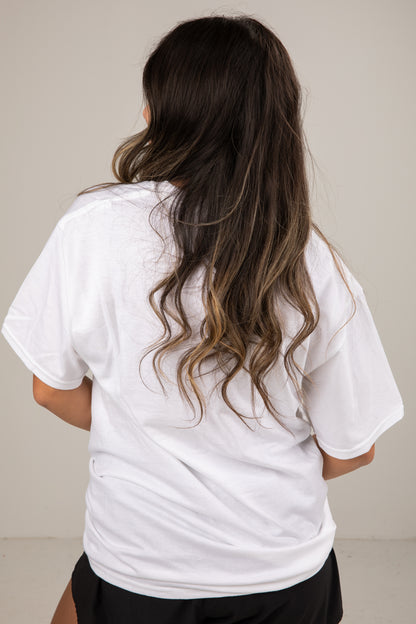 Person wearing a white t-shirt with long hair, standing against a plain background