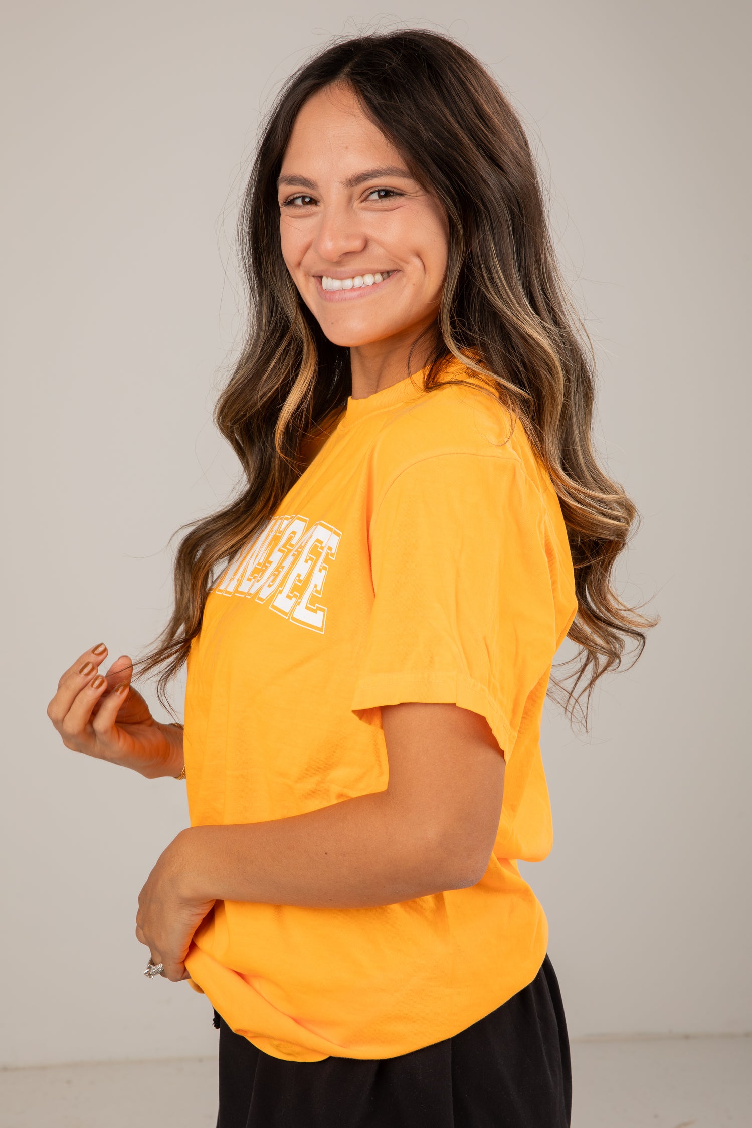 Woman wearing a bright orange t-shirt with text, standing against a plain background