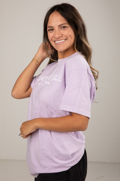 Woman wearing a light purple t-shirt with text on a plain background