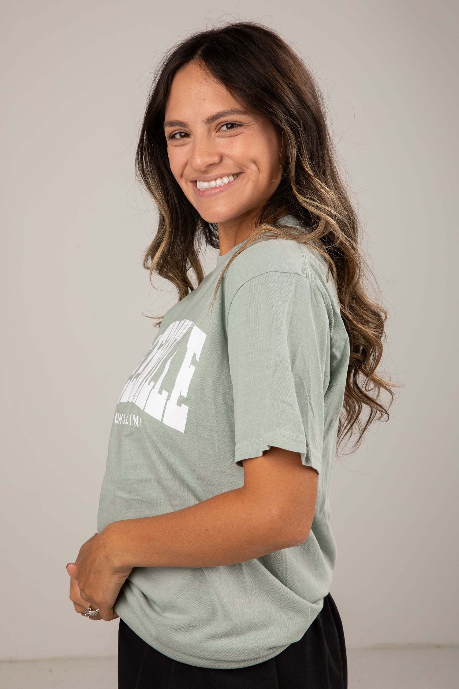 Woman wearing a light green t-shirt with text, standing against a plain background