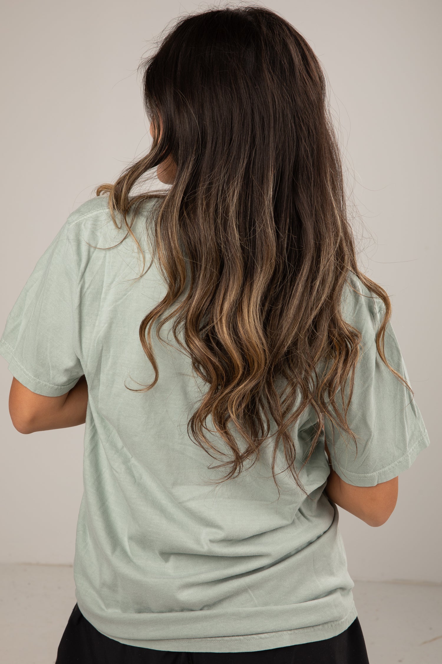 Person wearing a light green shirt with long, wavy hair on a plain background