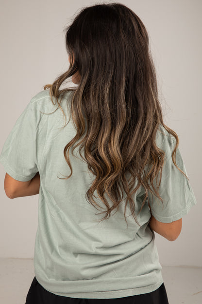 Person wearing a light green shirt with long, wavy hair on a plain background