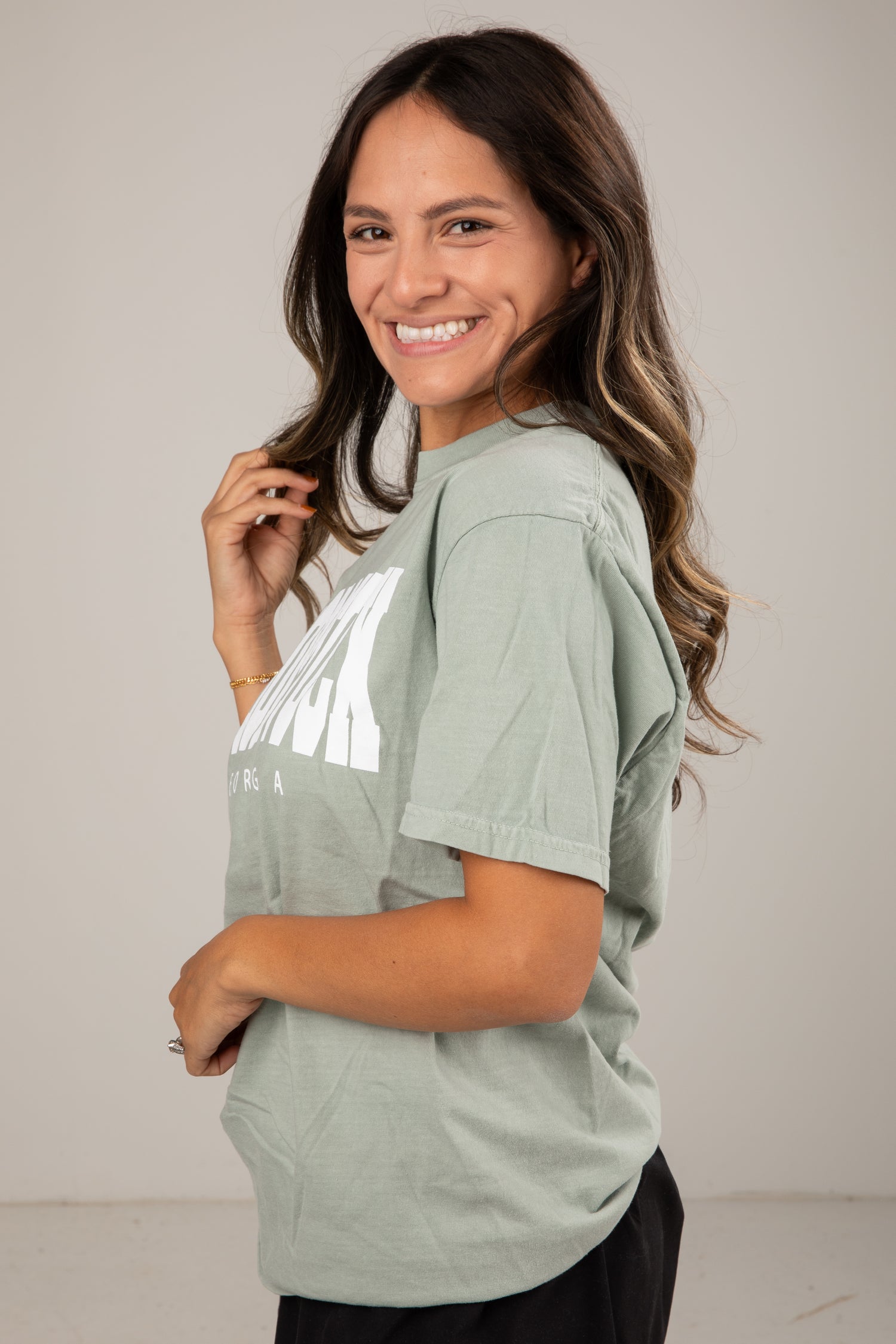 Woman wearing a light green t-shirt with a reflective design on a plain background