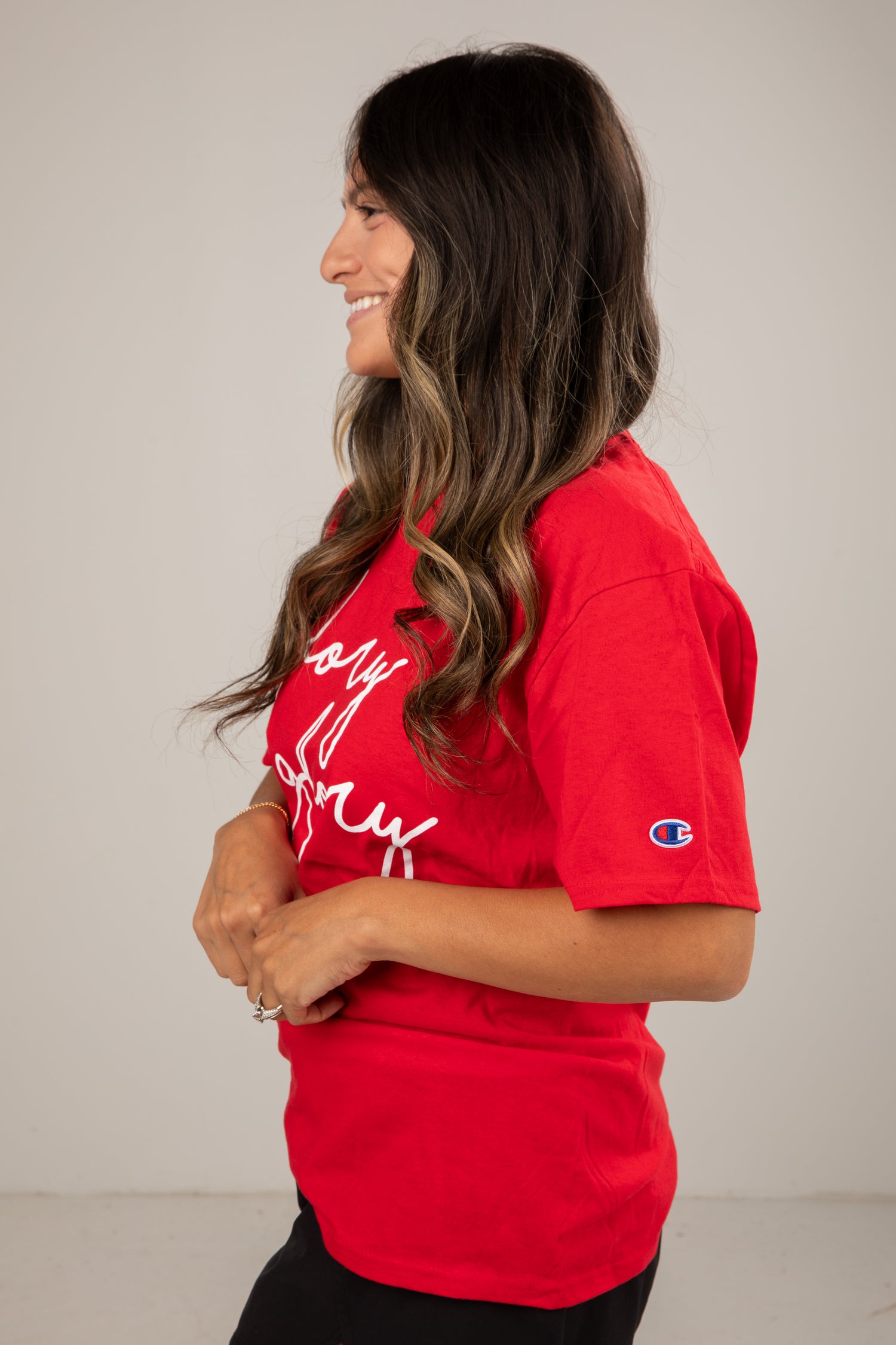 Woman wearing a red t-shirt with white text and a logo on a plain background
