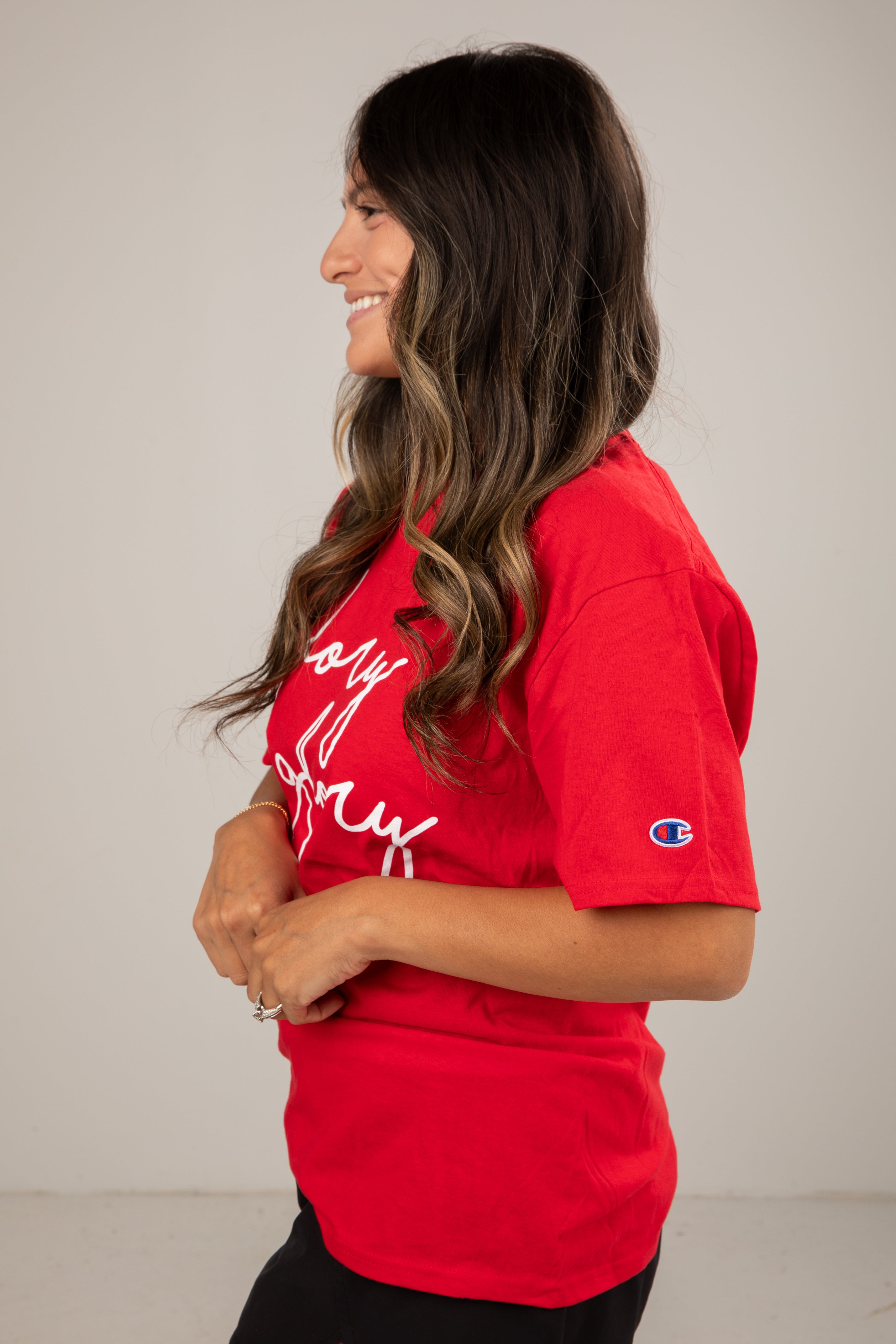 Woman wearing a red t-shirt with white text and a logo on a plain background