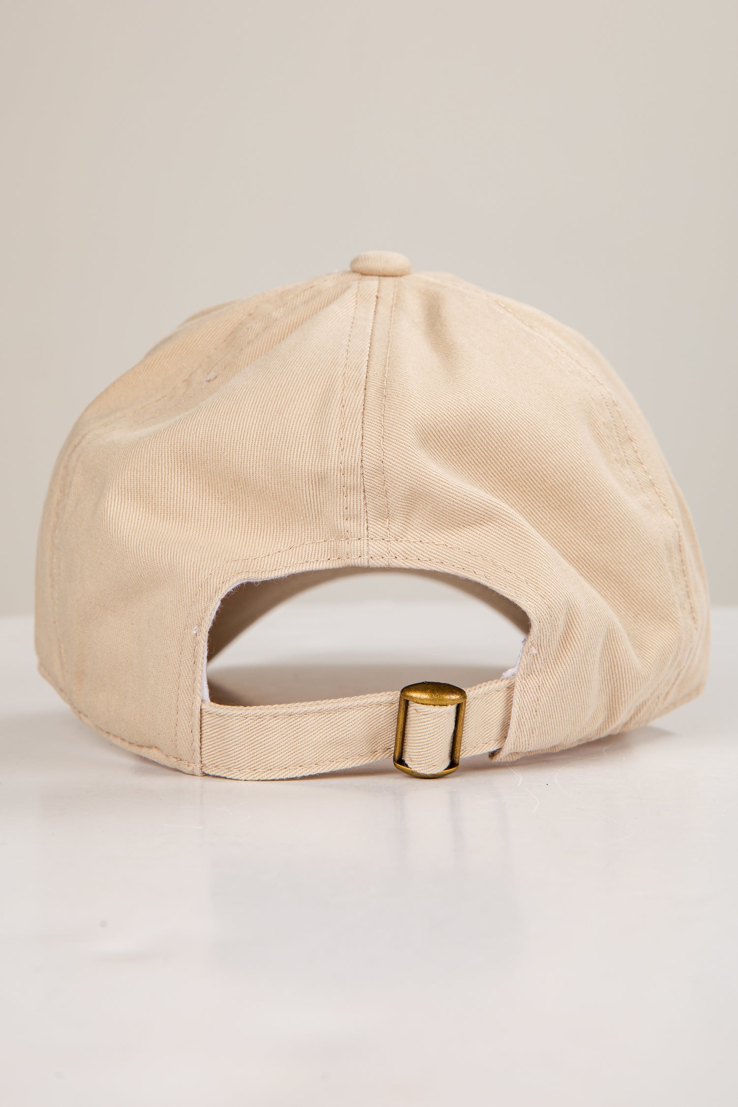 Beige cap with a gold buckle on a light gray background