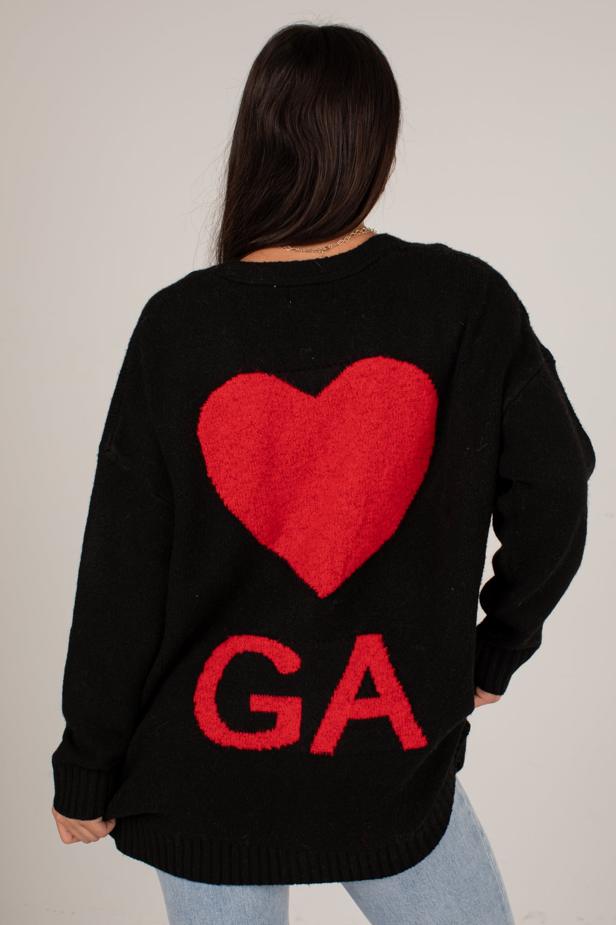 A woman viewed from behind wearing a black knit sweater with a large red heart and the letters &
