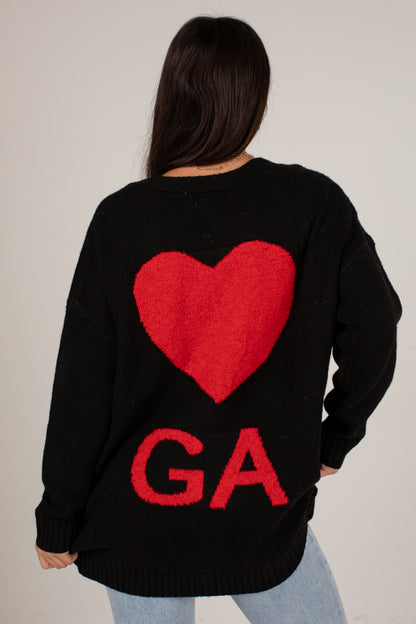 A woman viewed from behind wearing a black knit sweater with a large red heart and the letters &
