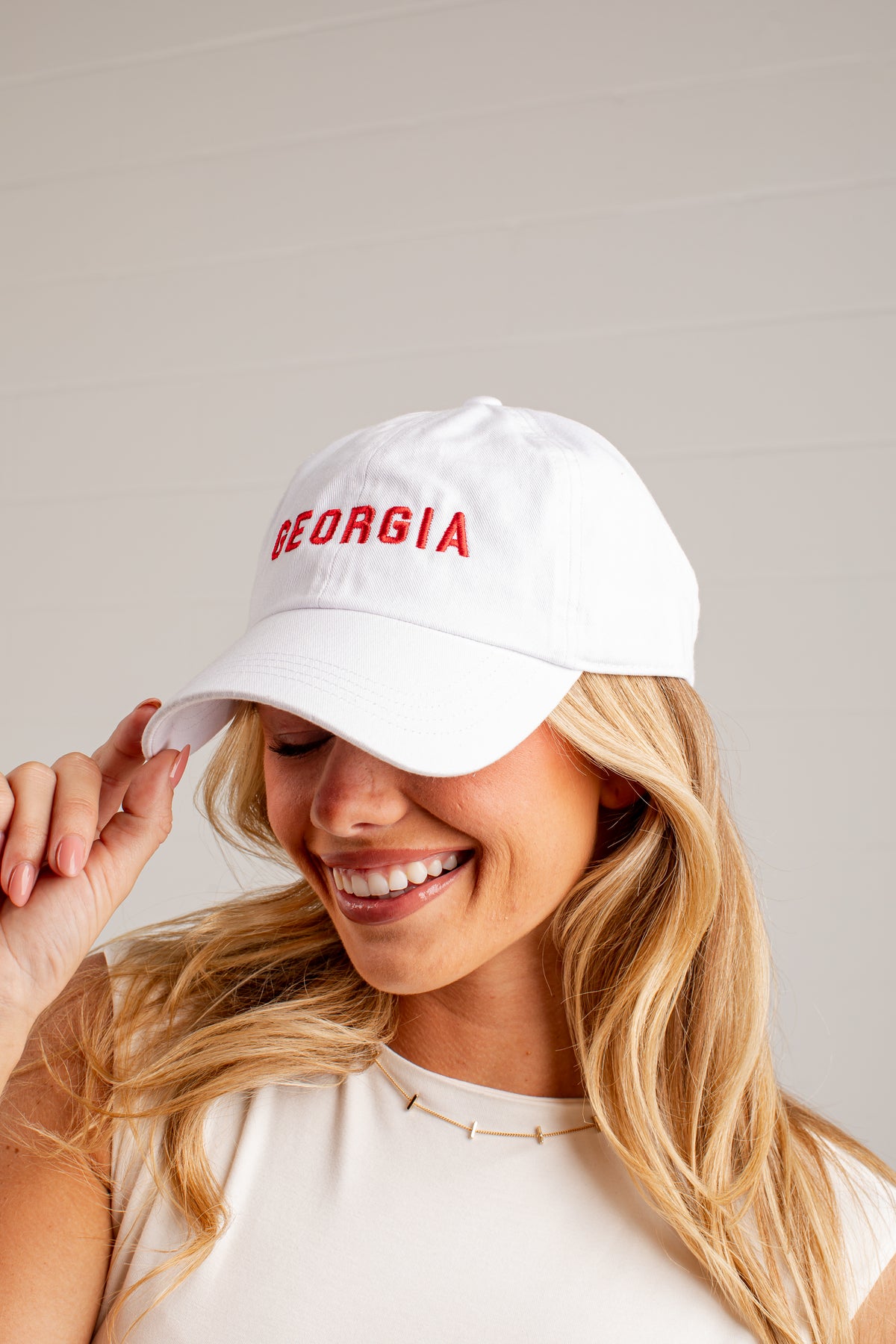 A smiling blonde woman wearing a white baseball cap with &