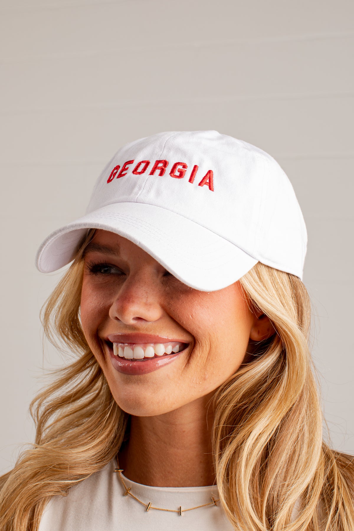A smiling blonde woman wearing a white baseball cap with &