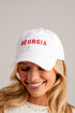 A smiling blonde woman wearing a white baseball cap with &