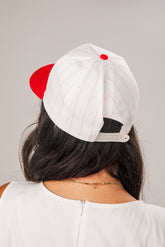 Person wearing a white cap with red accents on a plain background