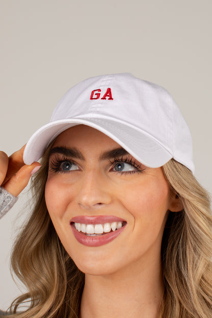 A smiling blonde woman wearing a white baseball cap with red embroidered letters &