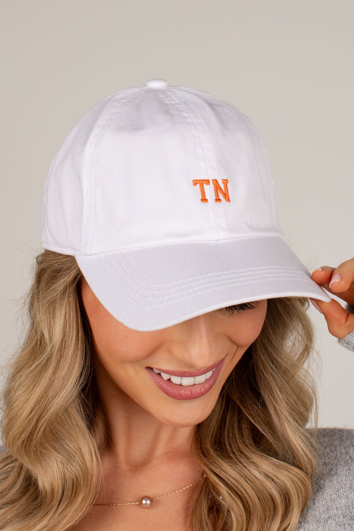 A woman wearing a white baseball cap with orange embroidered &
