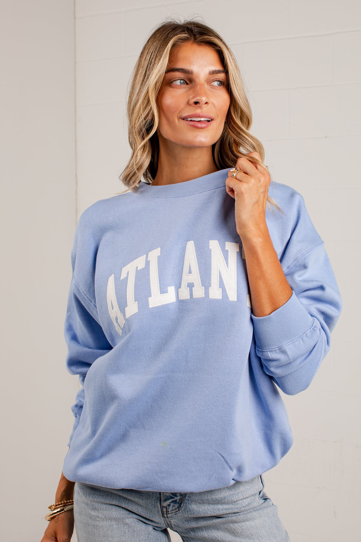 A woman wearing a light blue crewneck sweatshirt with &