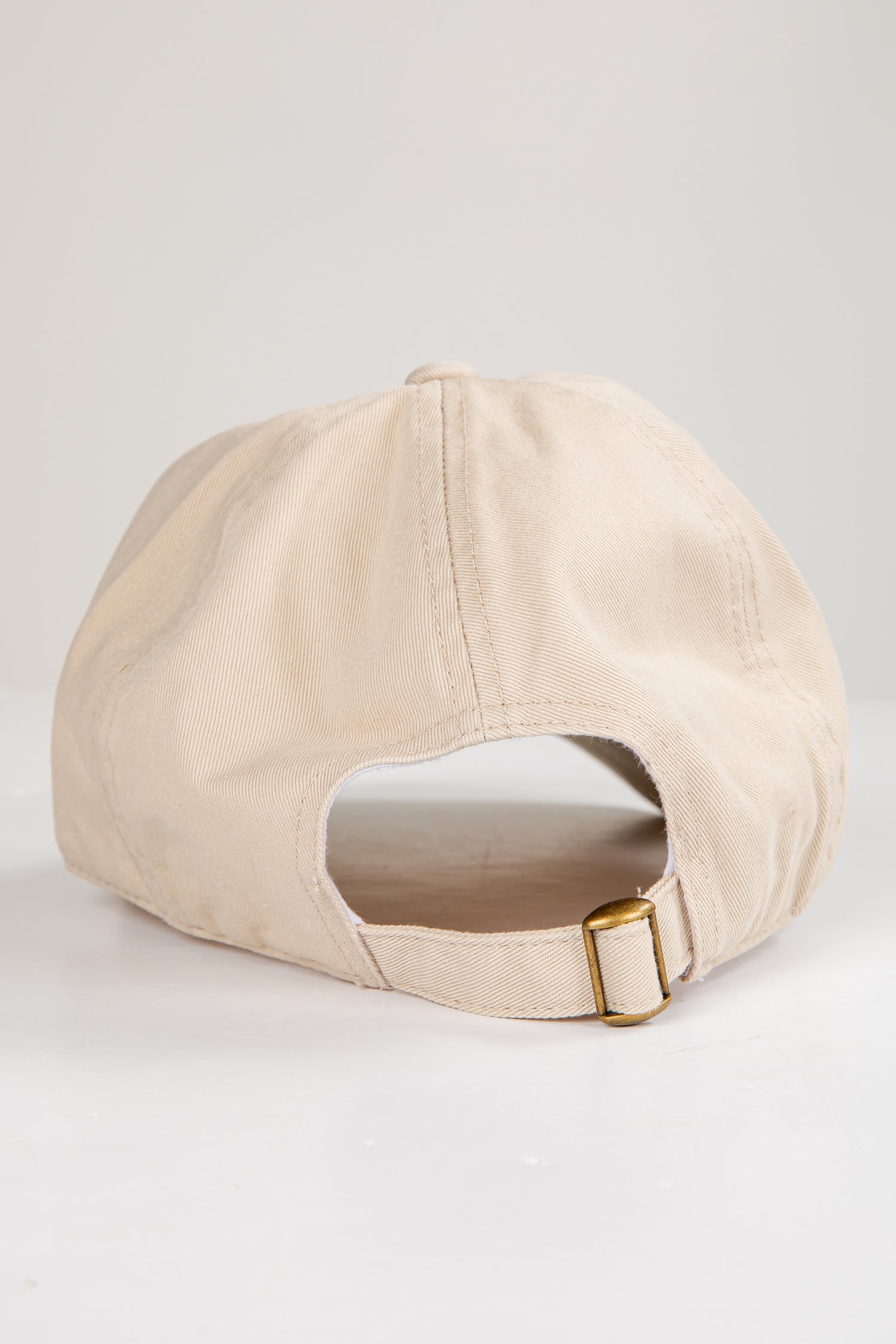 Beige baseball cap with a gold buckle on a light gray background