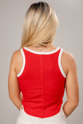 Person wearing a red tank top with white trim on a gray background