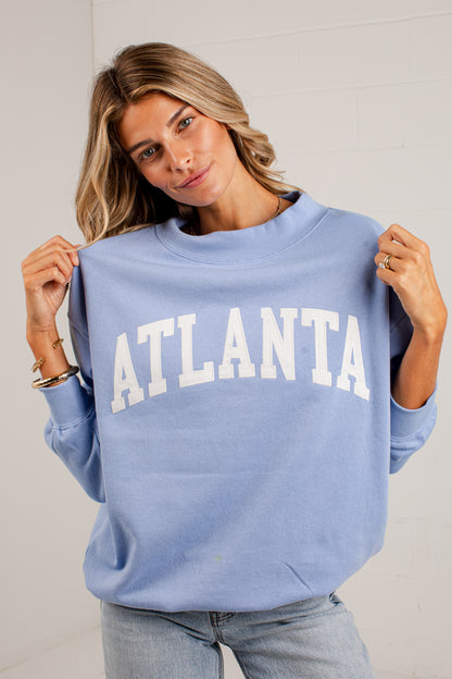 A woman wearing a light blue crewneck sweatshirt with &
