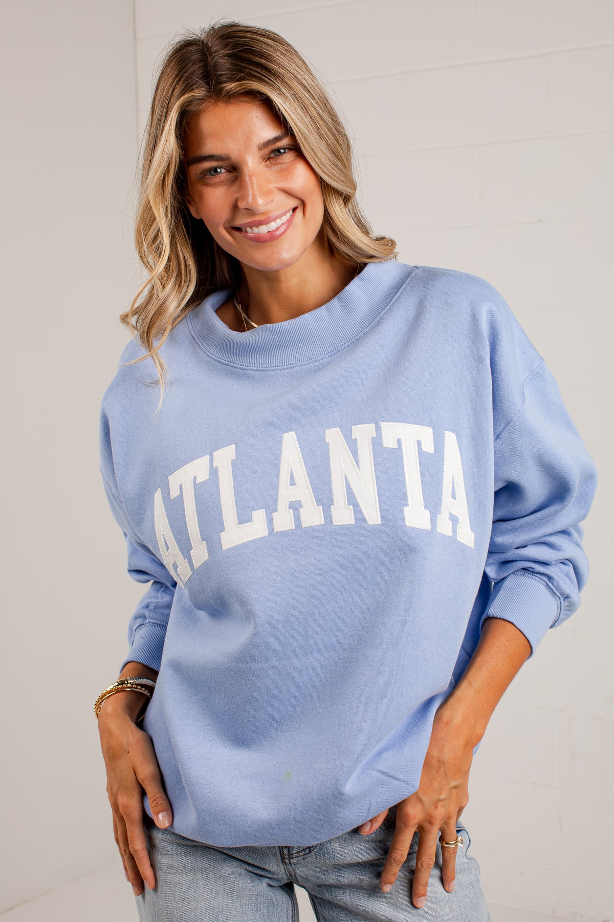 A woman wearing a light blue crewneck sweatshirt with &