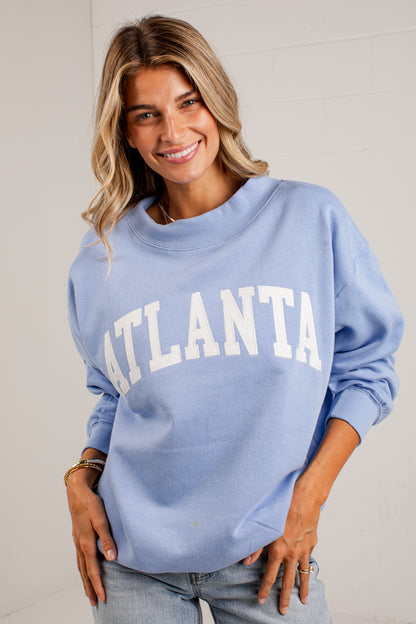 A woman wearing a light blue crewneck sweatshirt with &