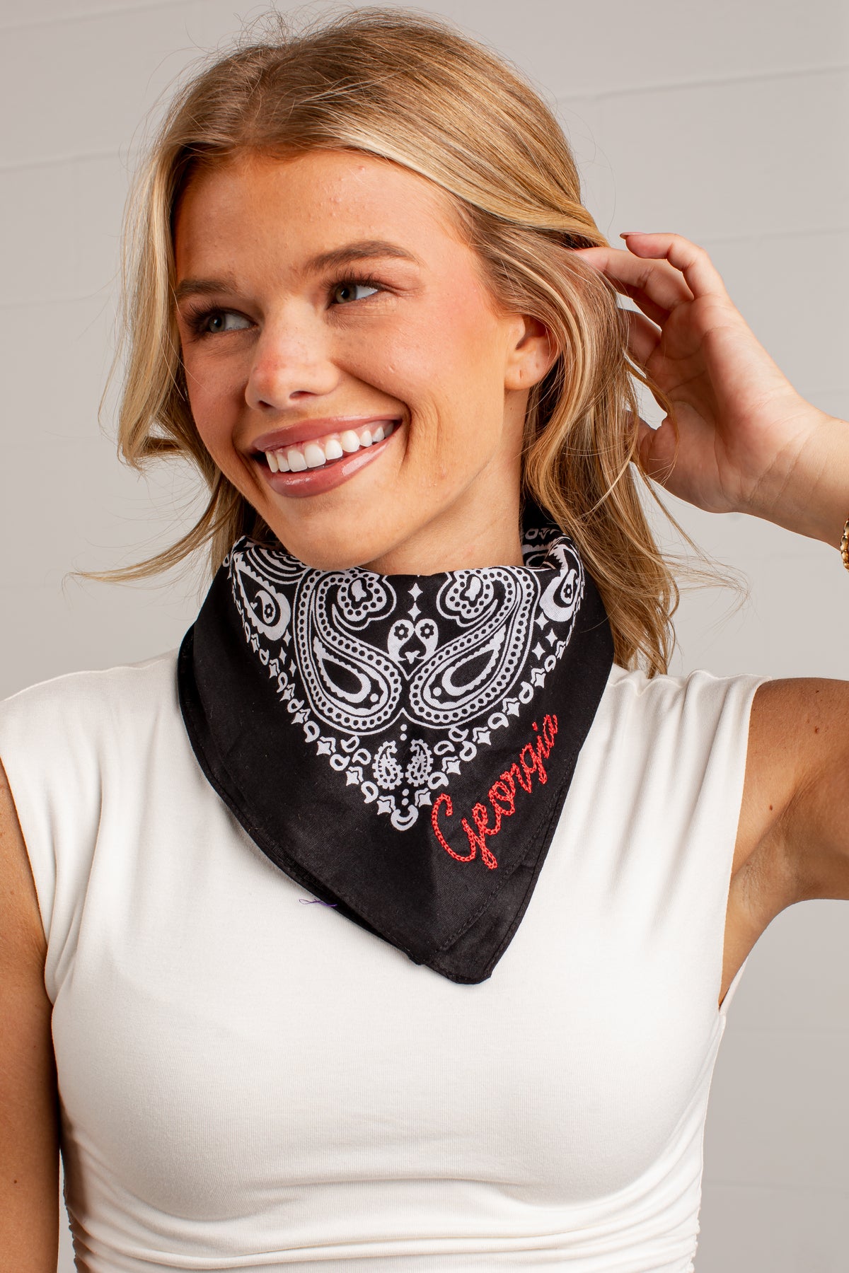 A smiling blonde woman wearing a black bandana with a white paisley pattern and the name &