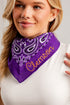 A close-up of a woman wearing a purple bandana bib with a paisley pattern and the name &