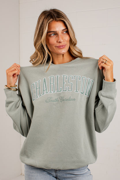 A woman wearing a sage green sweatshirt with &