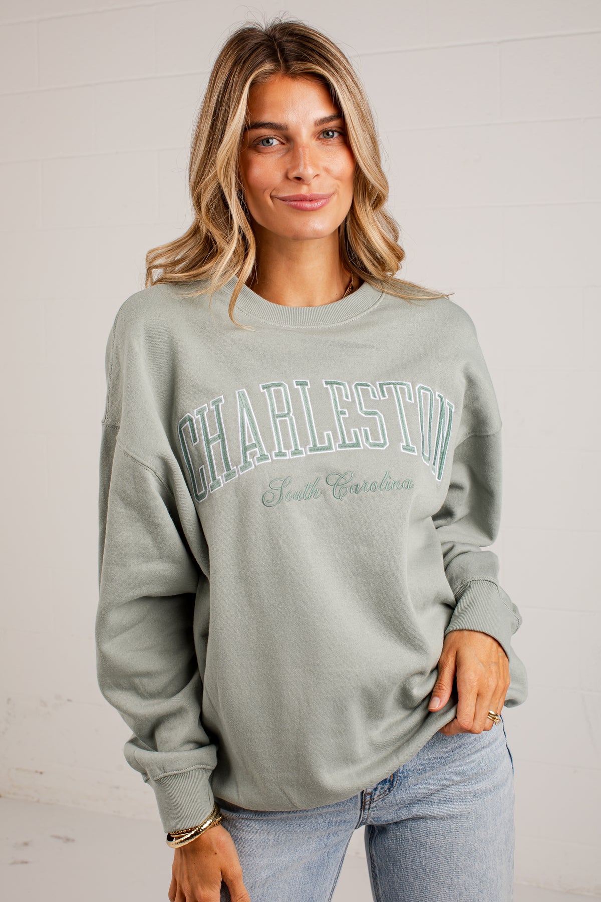 A woman wearing a sage green crewneck sweatshirt with &