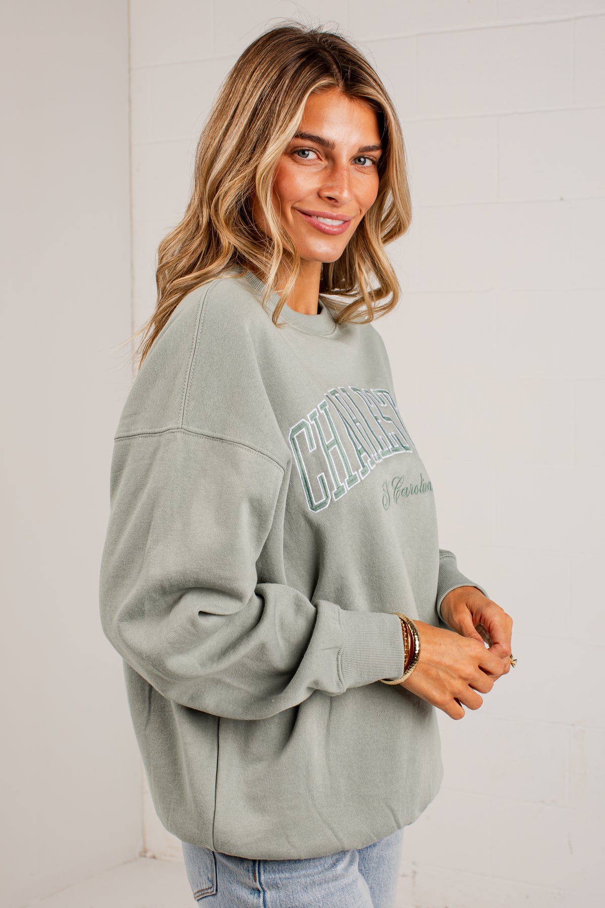 A woman wearing a sage green crewneck sweatshirt with &