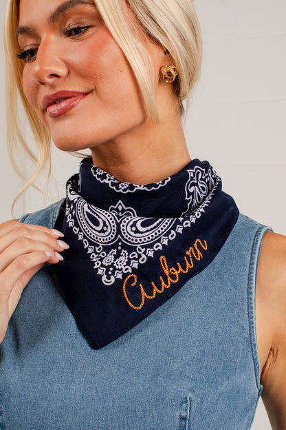 A close-up of a woman wearing a navy blue bandana with a white paisley pattern and the word &
