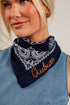 A close-up of a woman wearing a navy blue bandana with a white paisley pattern and the word &