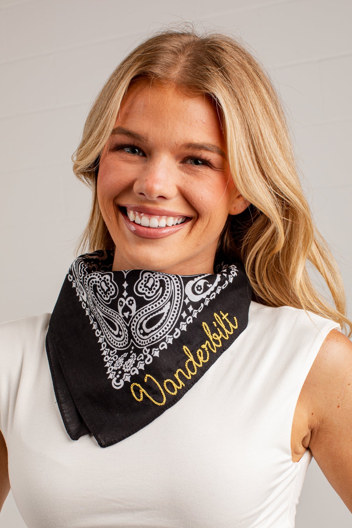 A smiling blonde woman wearing a black bandana with a white paisley pattern and the word &