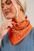 A close-up lifestyle shot of a woman wearing a bright orange bandana with a paisley pattern and the name &