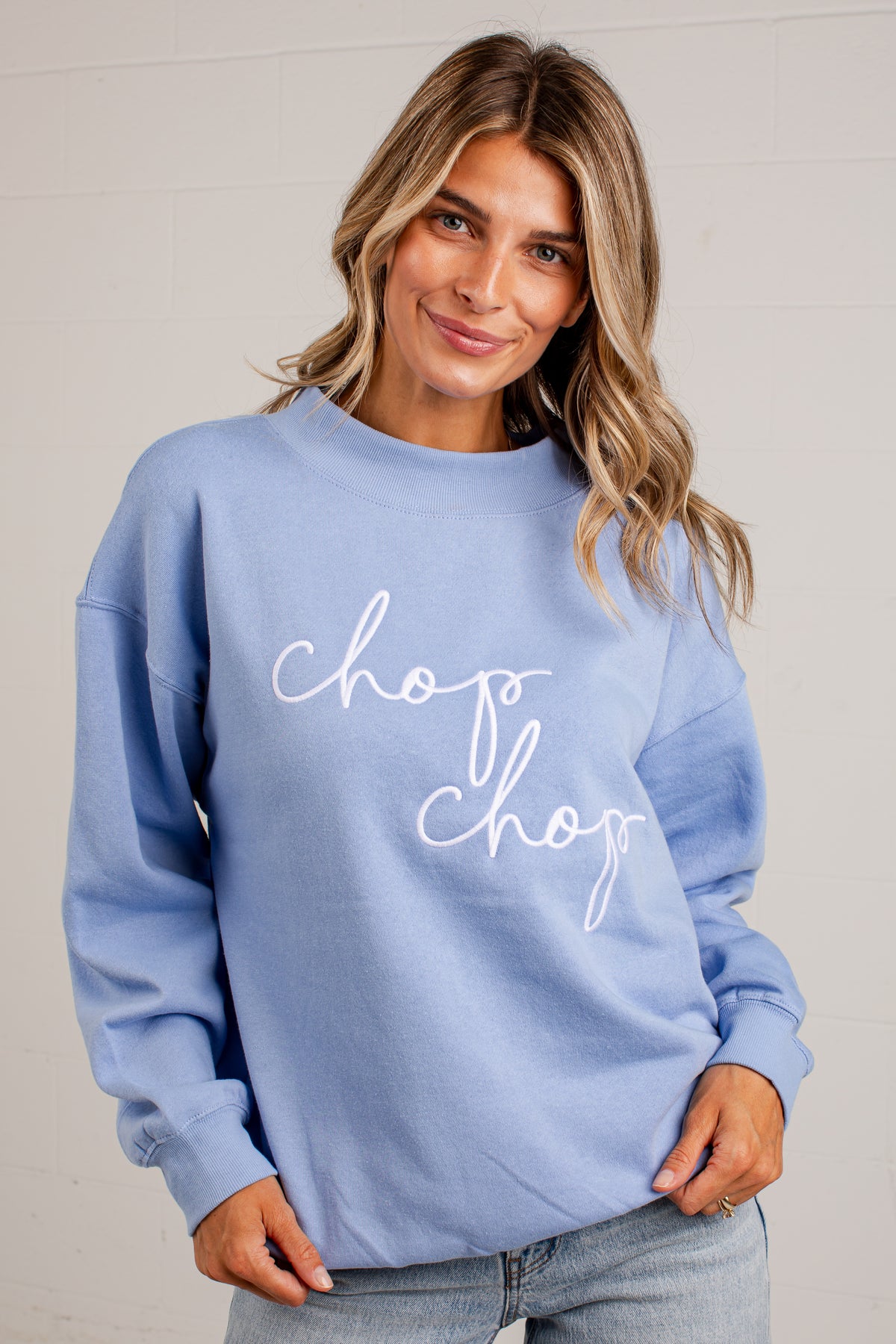 A woman wearing a light blue crewneck sweatshirt with &
