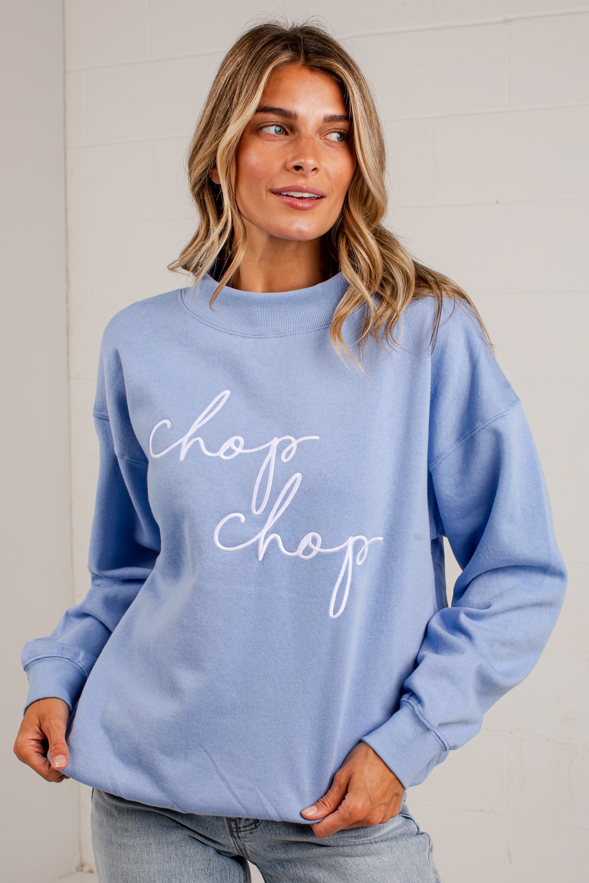 A woman wearing a light blue crewneck sweatshirt with &