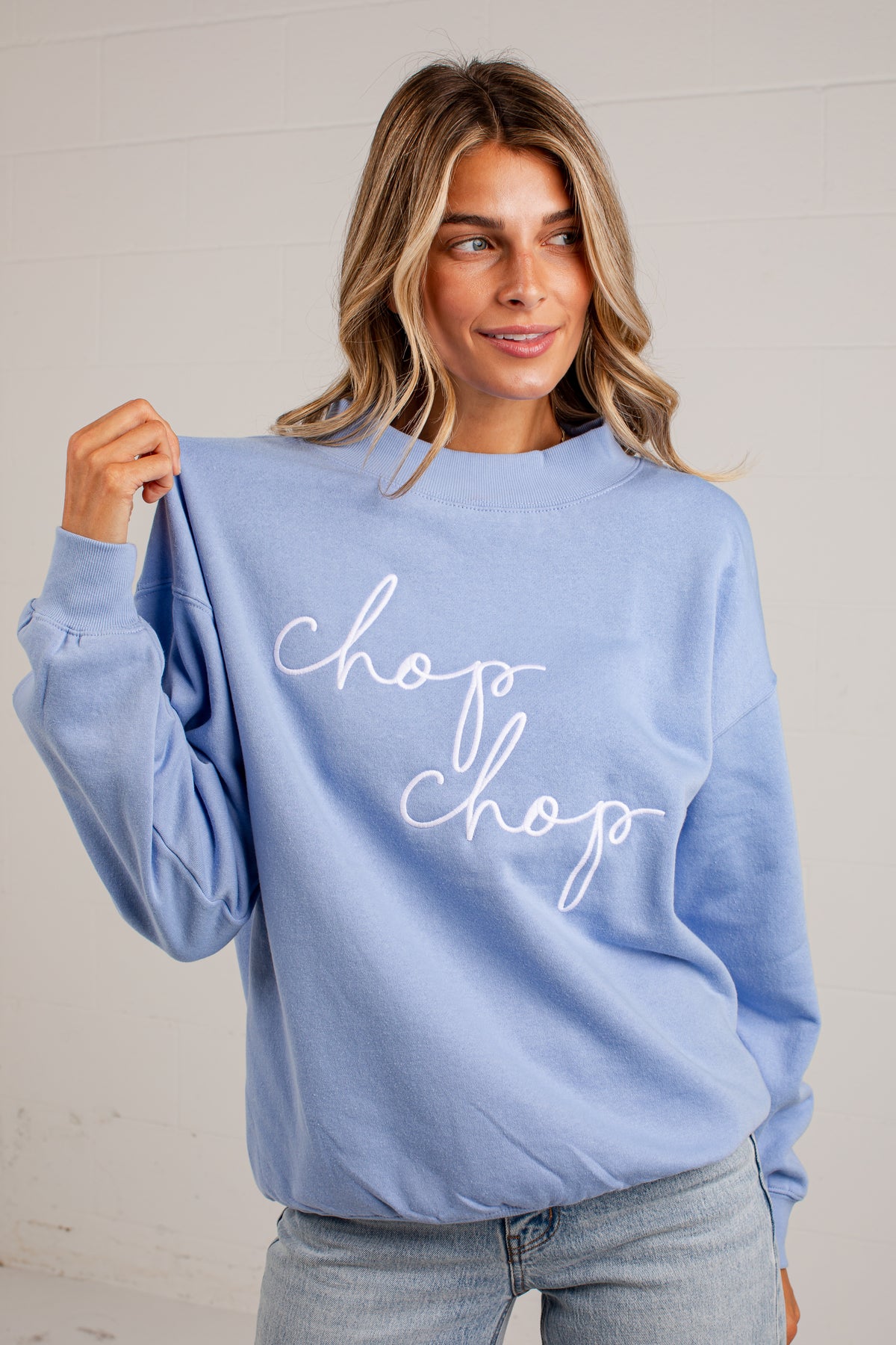 A woman wearing a light blue crewneck sweatshirt with &