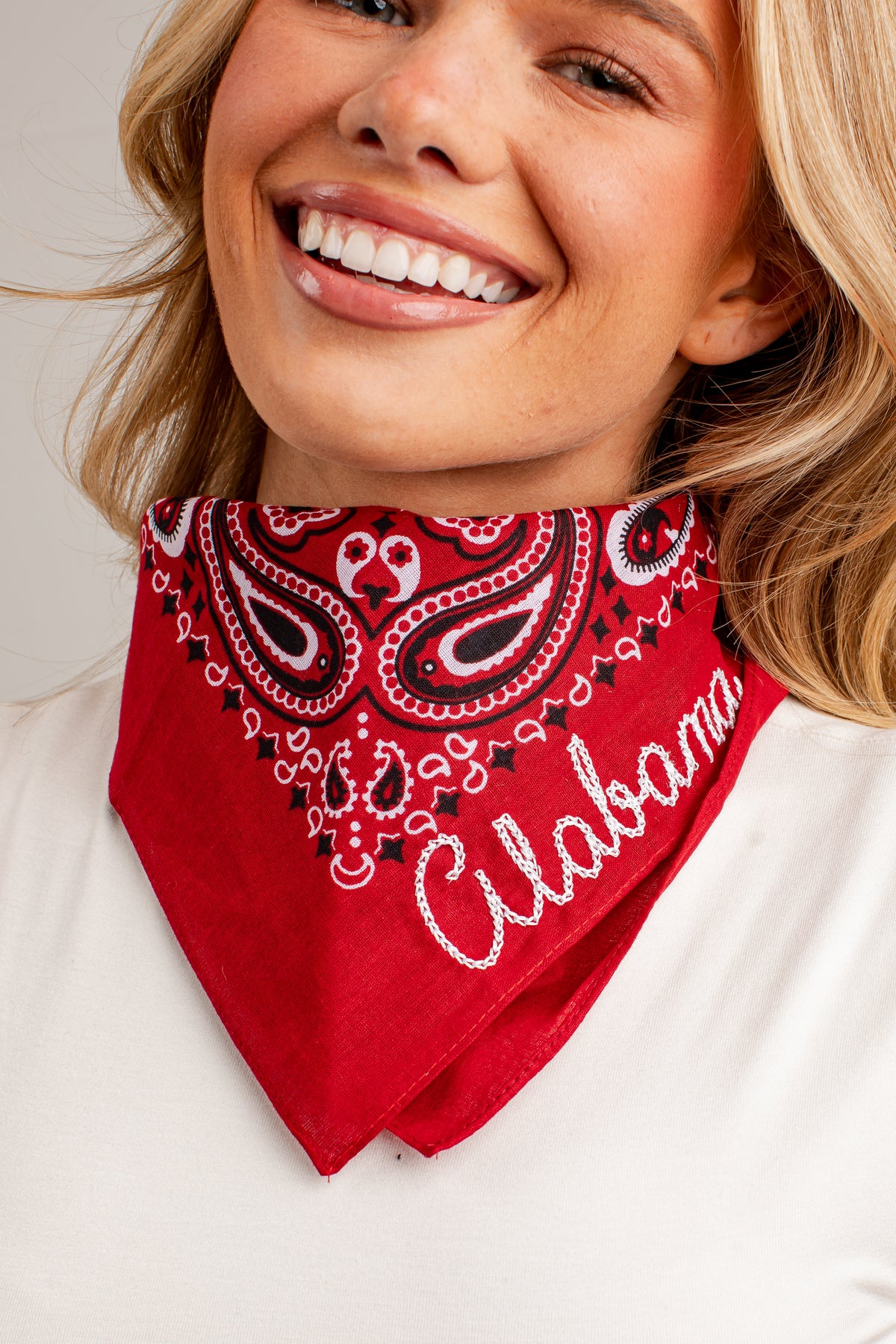A smiling blonde woman wearing a red bandana with a white and black paisley pattern and the word &