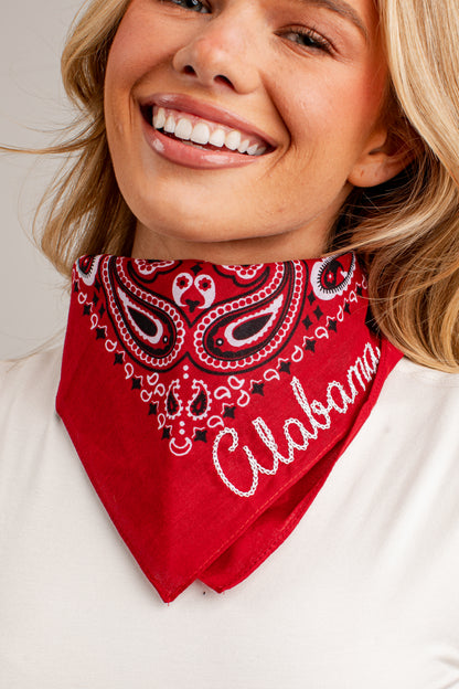 A smiling blonde woman wearing a red bandana with a white and black paisley pattern and the word &