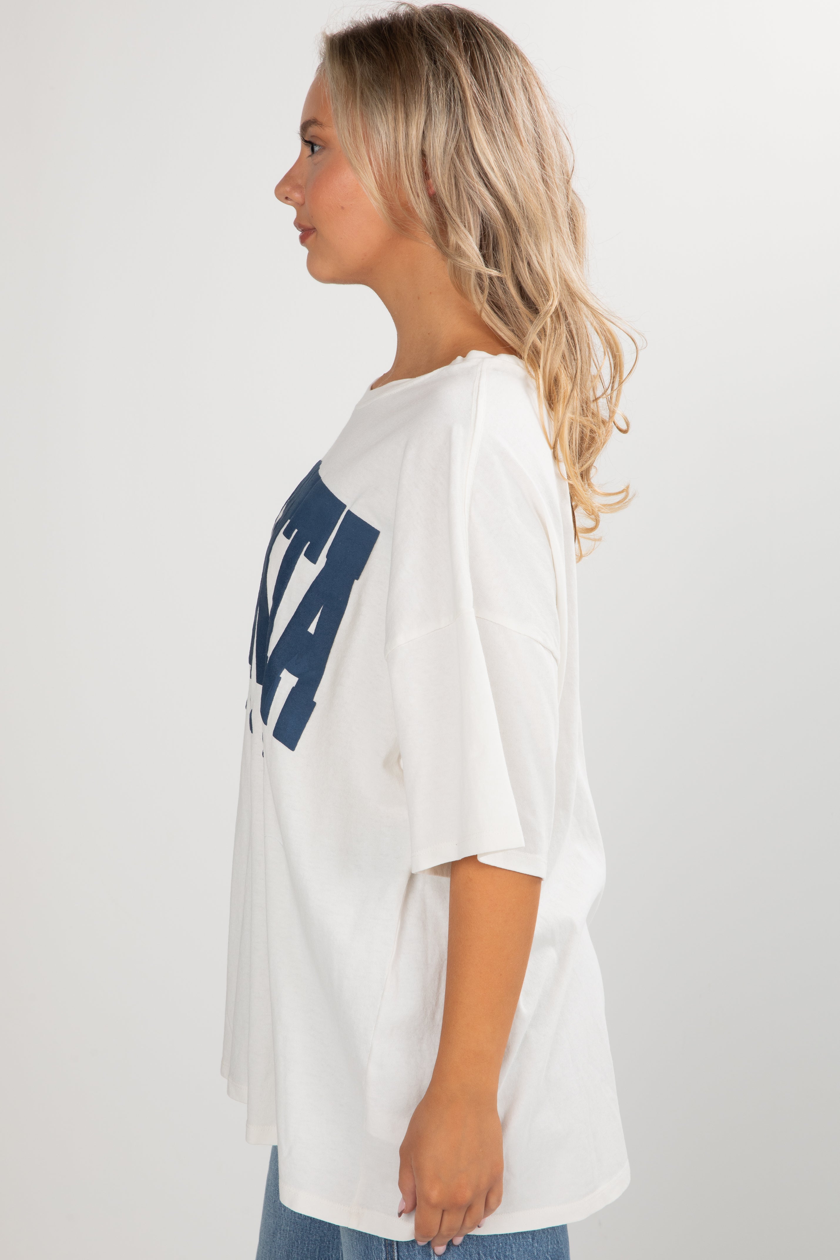 Woman wearing a white oversized t-shirt with blue text on a plain background