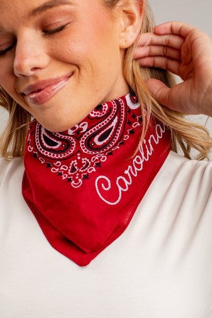 A close-up of a woman wearing a red bandana with a white and black paisley pattern and the word &