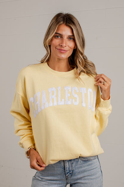 A woman wearing a pale yellow crewneck sweatshirt with &