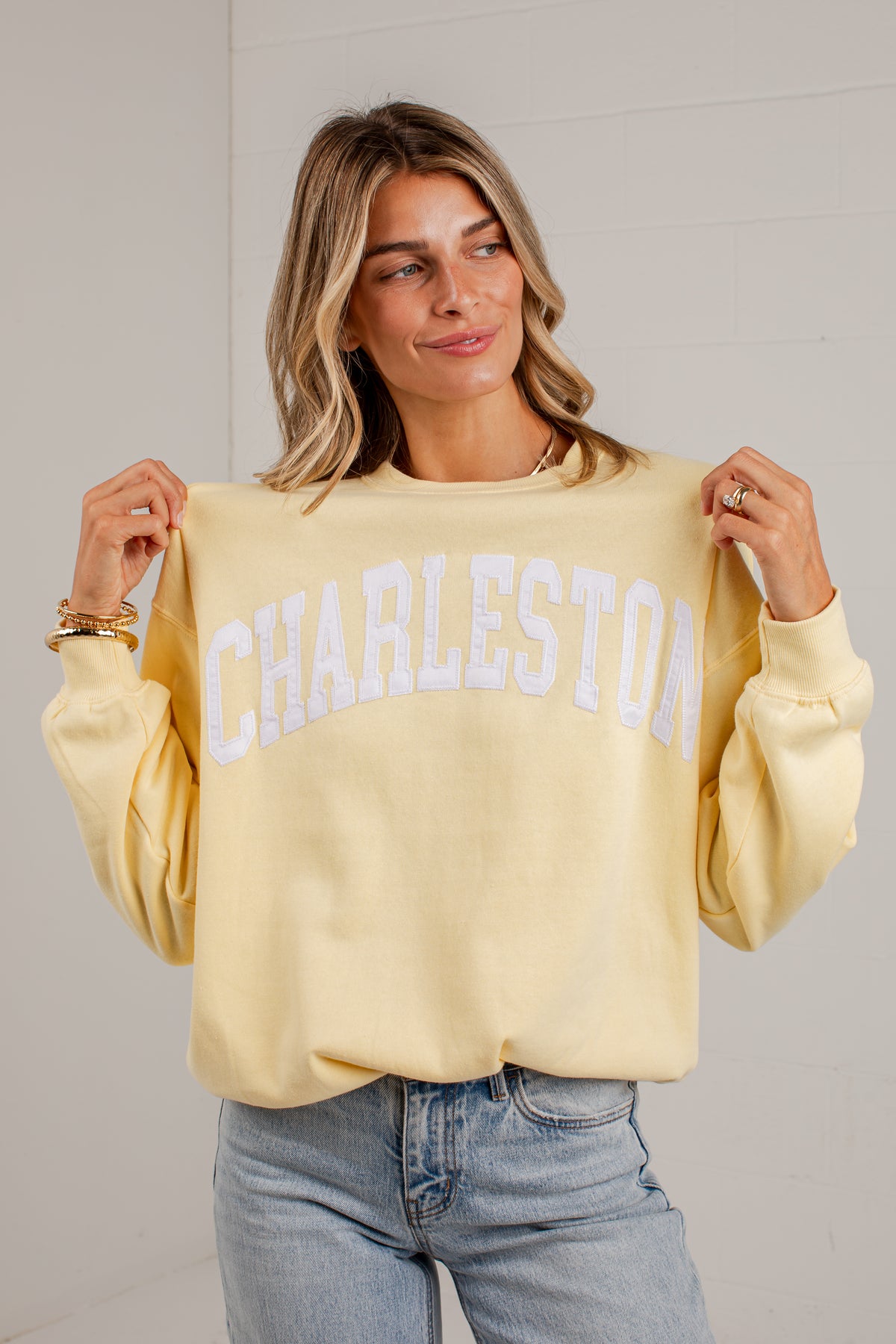 A woman wearing a pale yellow crewneck sweatshirt with &