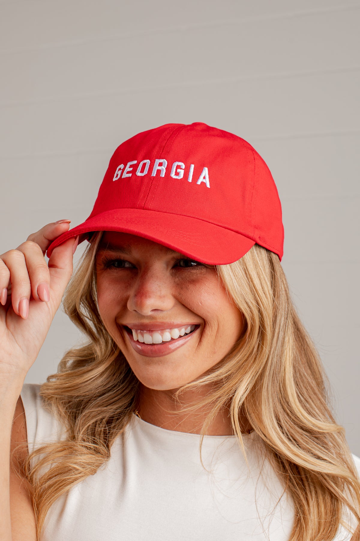 A smiling blonde woman wearing a bright red baseball cap with &