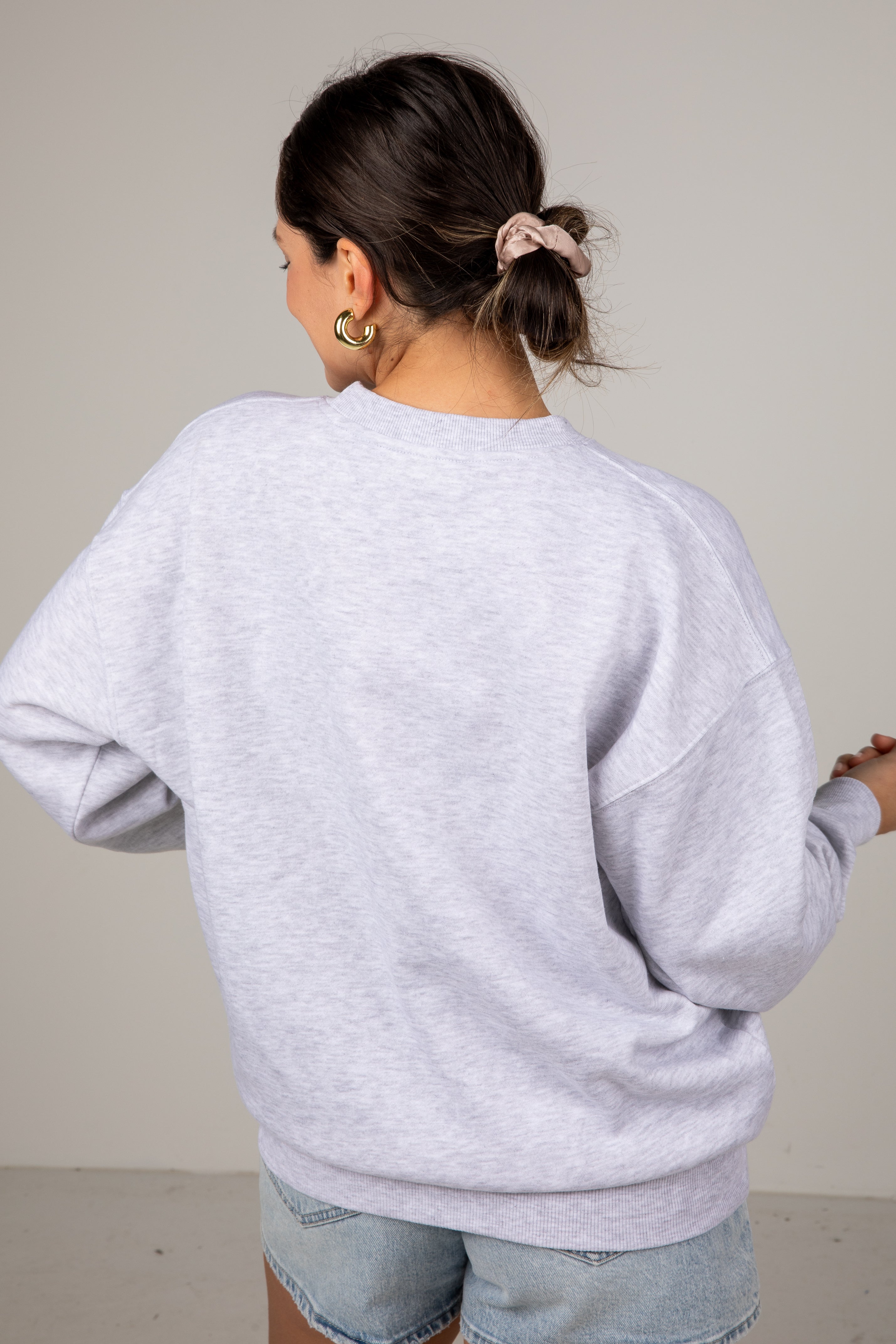 Person wearing a light gray sweatshirt and light blue jeans against a plain background