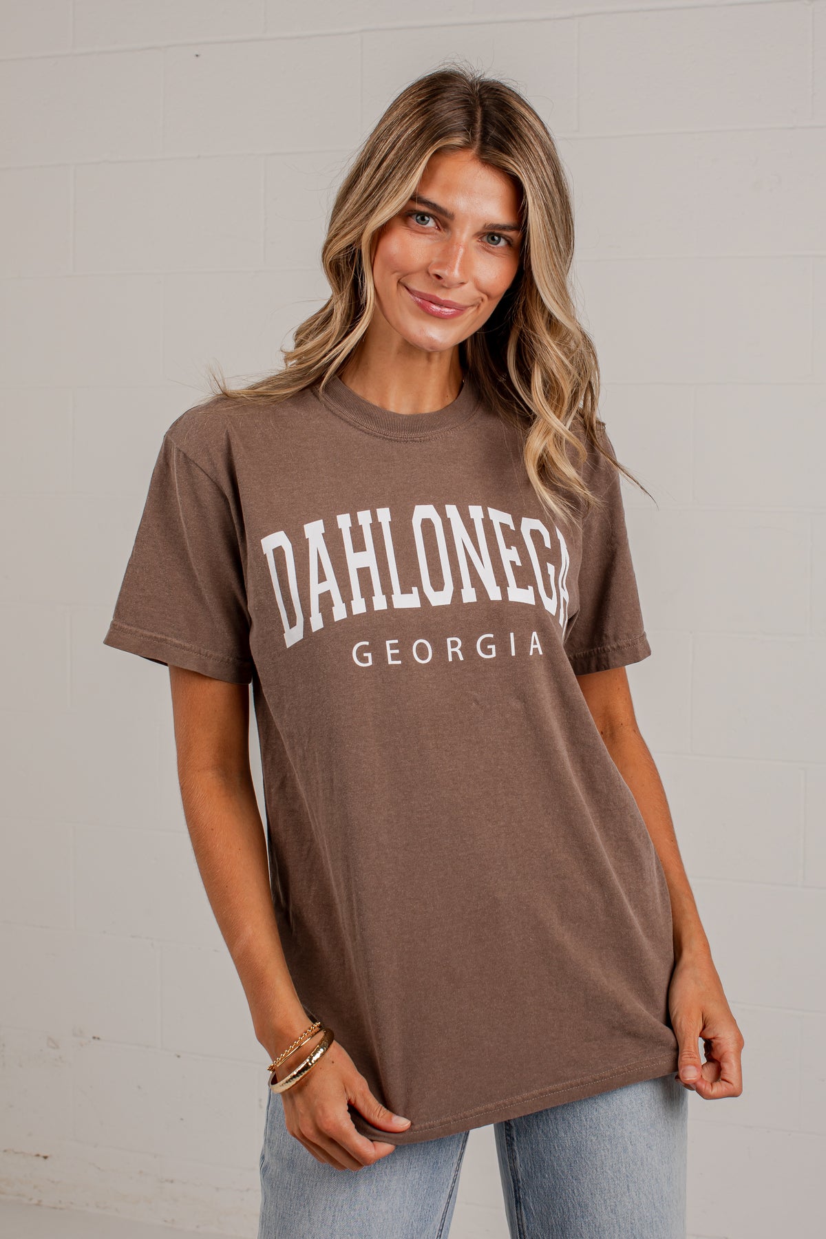 A woman wearing a brown short-sleeve graphic t-shirt with &