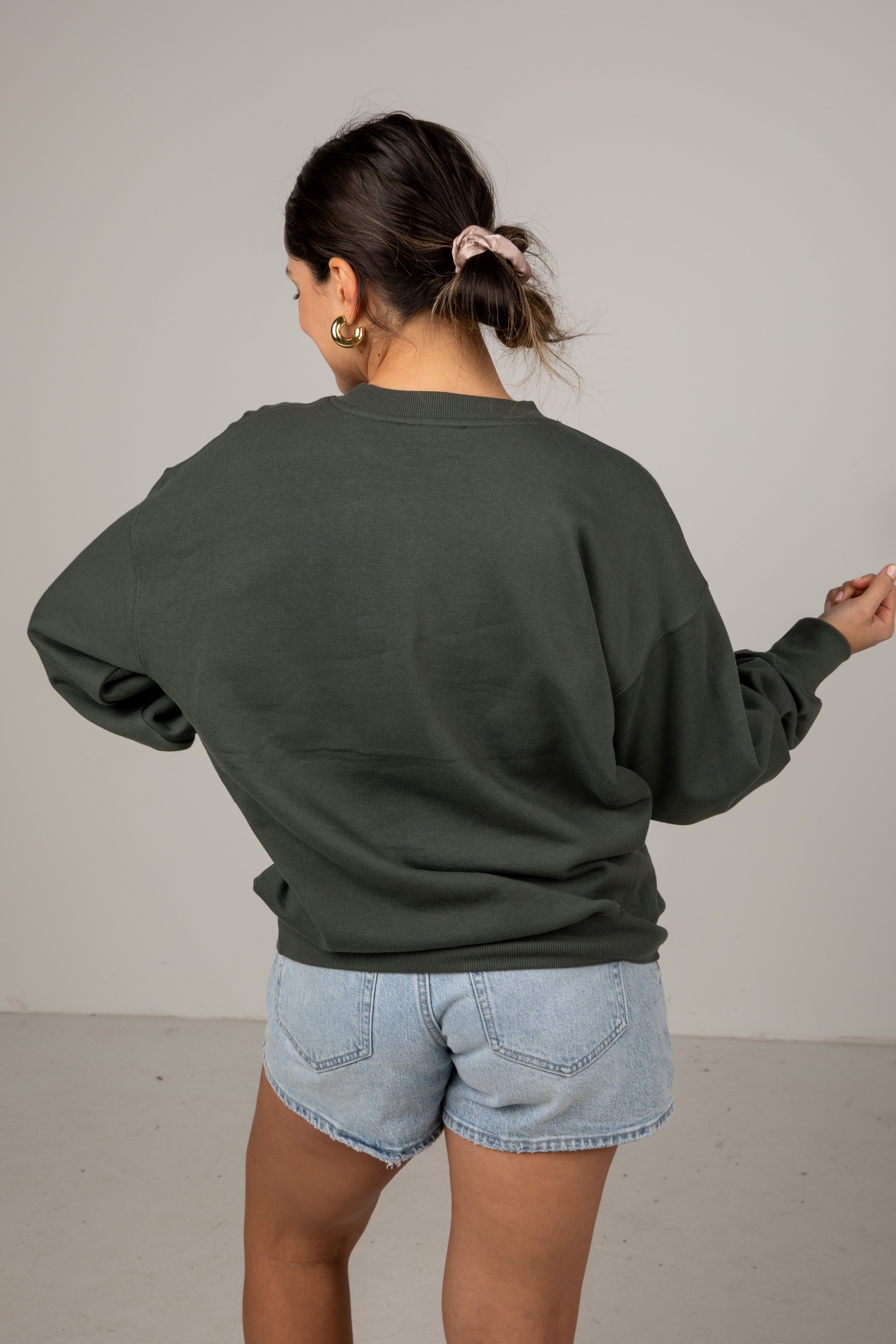 Person wearing a green sweatshirt and light blue shorts against a plain background